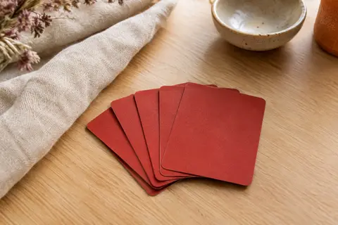 Jeu de cartes rouge posé en éventail sur une table en bois clair avec du lin et une céramique