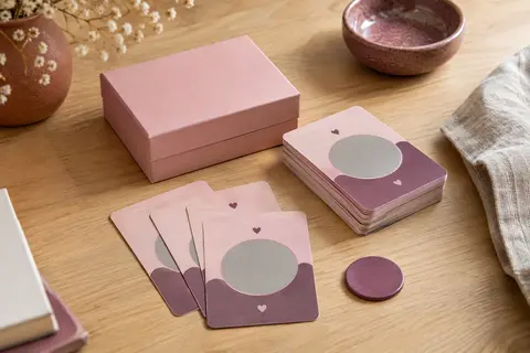 Jeu de cartes à gratter rose pour couples, accompagné de son jeton sur une table en bois clair