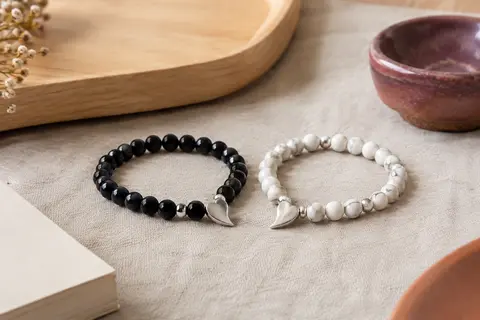 Deux bracelets assortis à perles noires et blanches avec des motifs argentés en demi-cœur
